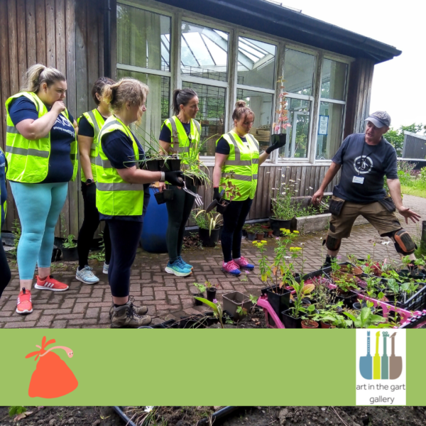 A group of people with light skin tone, wearing high vis jackets, standing in a garden space in front of growing plots. Logo: Art in the Gart A group of people with light skin tone, wearing high vis jackets, standing in a garden space in front of growing plots. Logo: Art in the Gart