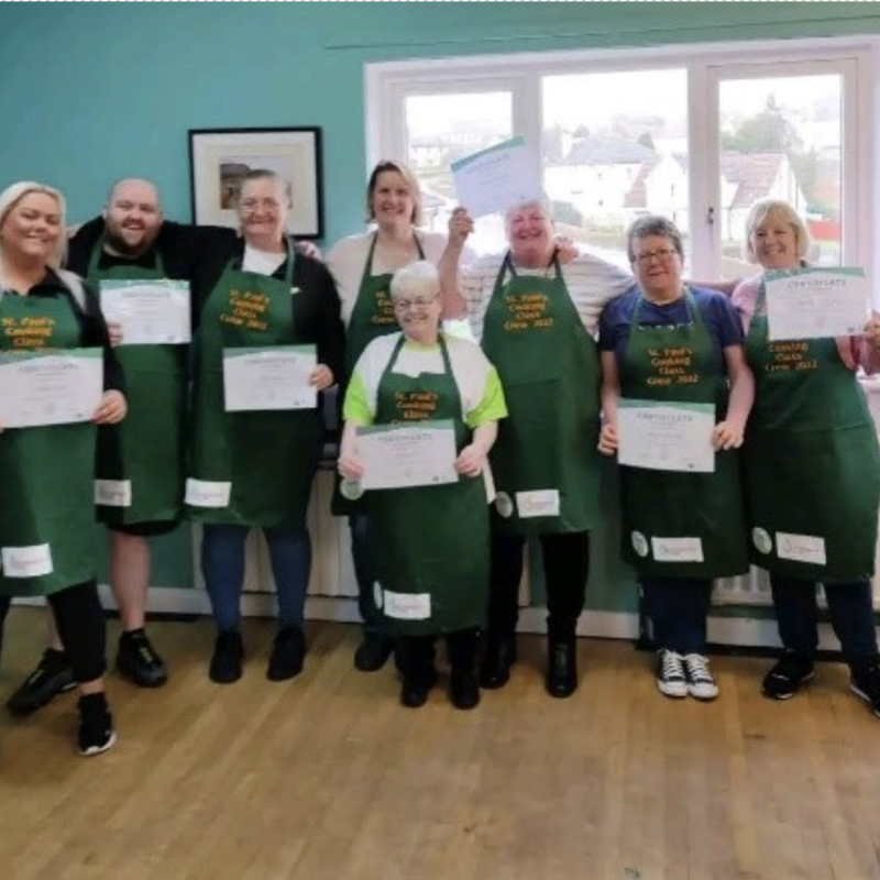A group photo of the cooking crew wearing their aprons and holding certificates. All the people in the photo have a light skin tone. A group photo of the cooking crew wearing their aprons and holding certificates. All the people in the photo have a light skin tone.